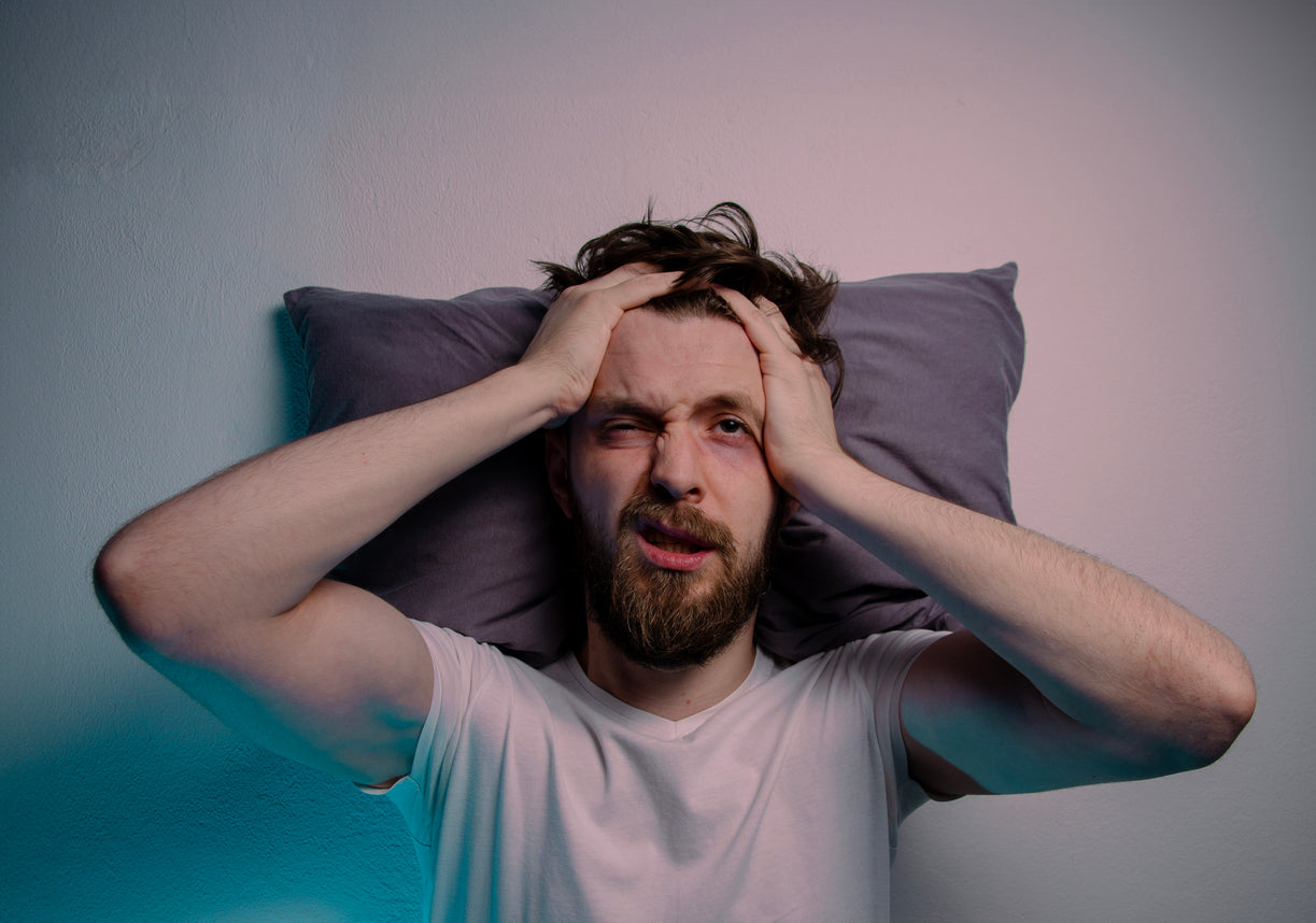 Man lying in bed with hands on head, looking distressed.