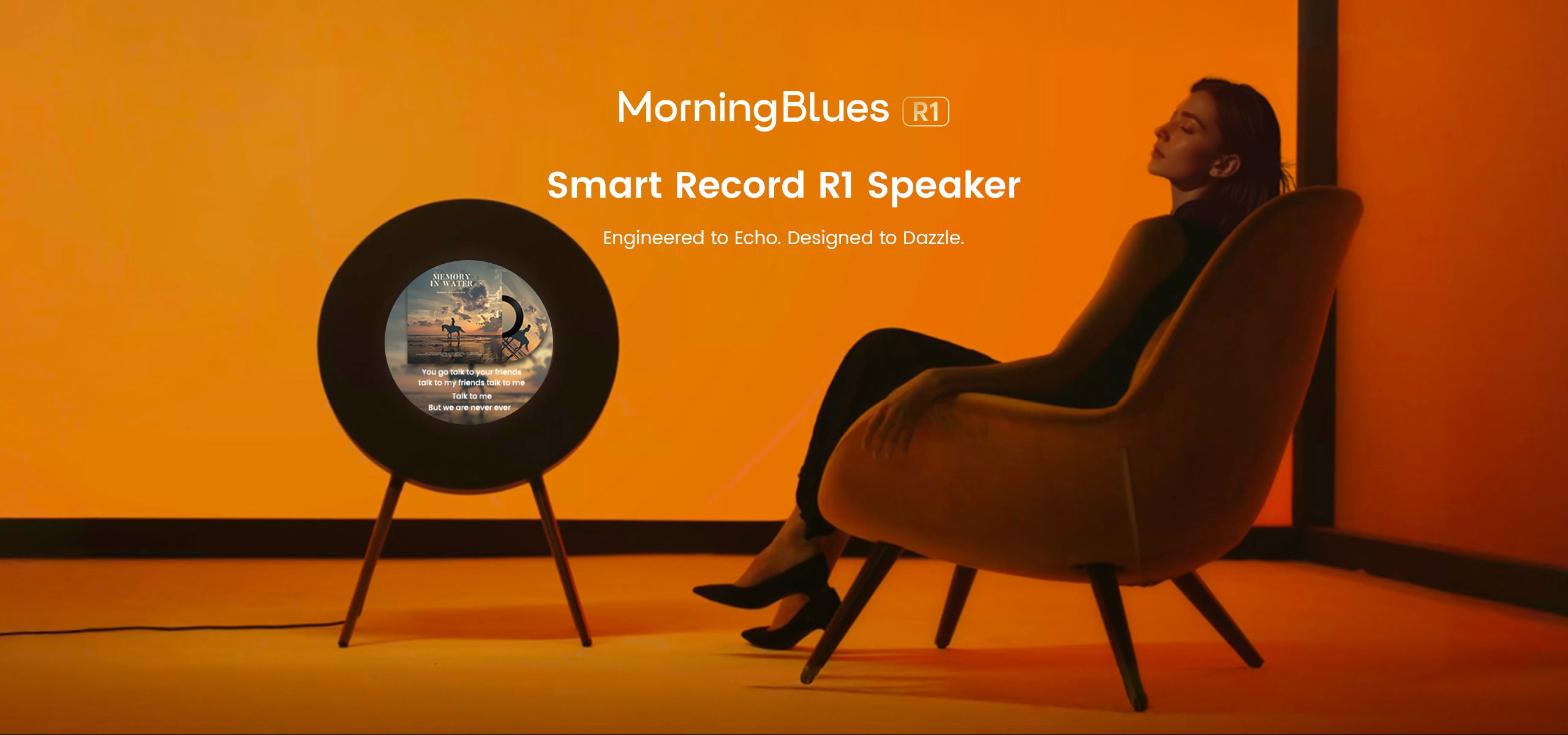 Person sitting in a chair next to a smart record R1 speaker with 'MorningBlues' branding on an orange background.