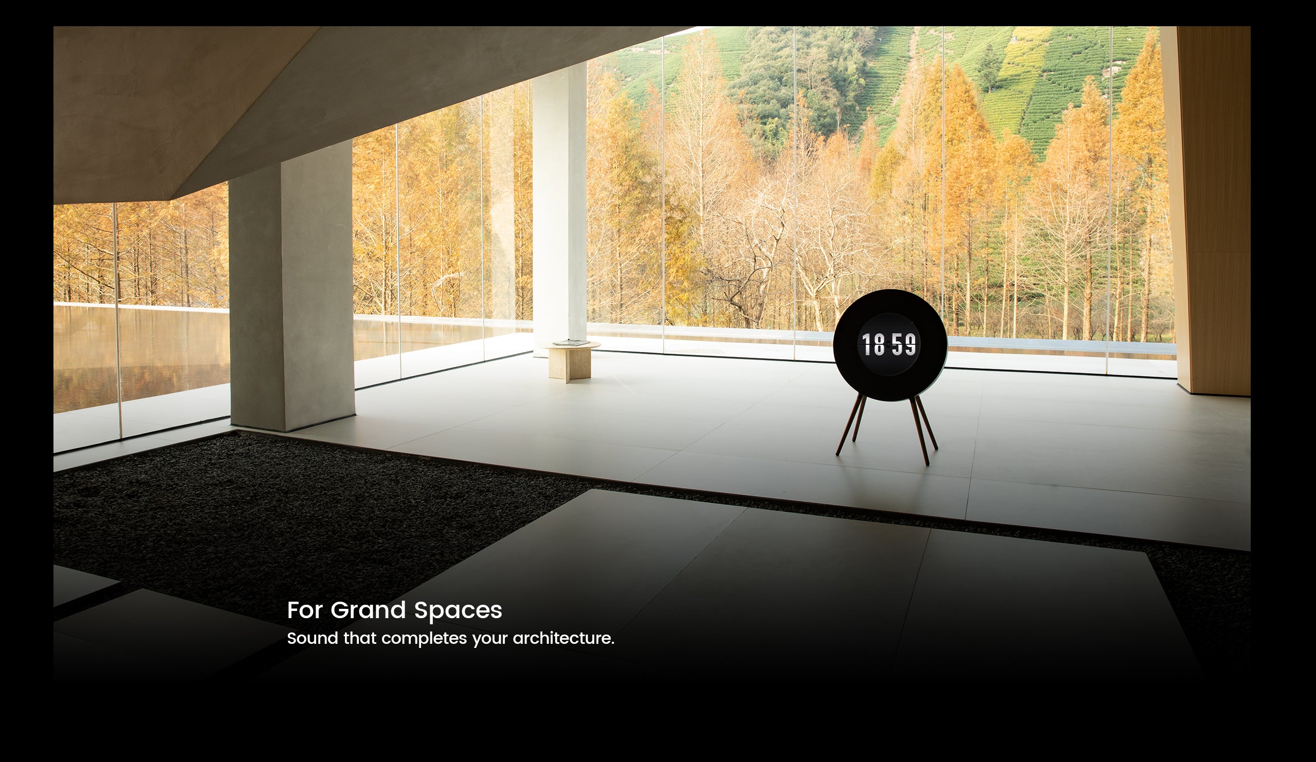 Modern room with large windows showing trees, featuring a black speaker.
