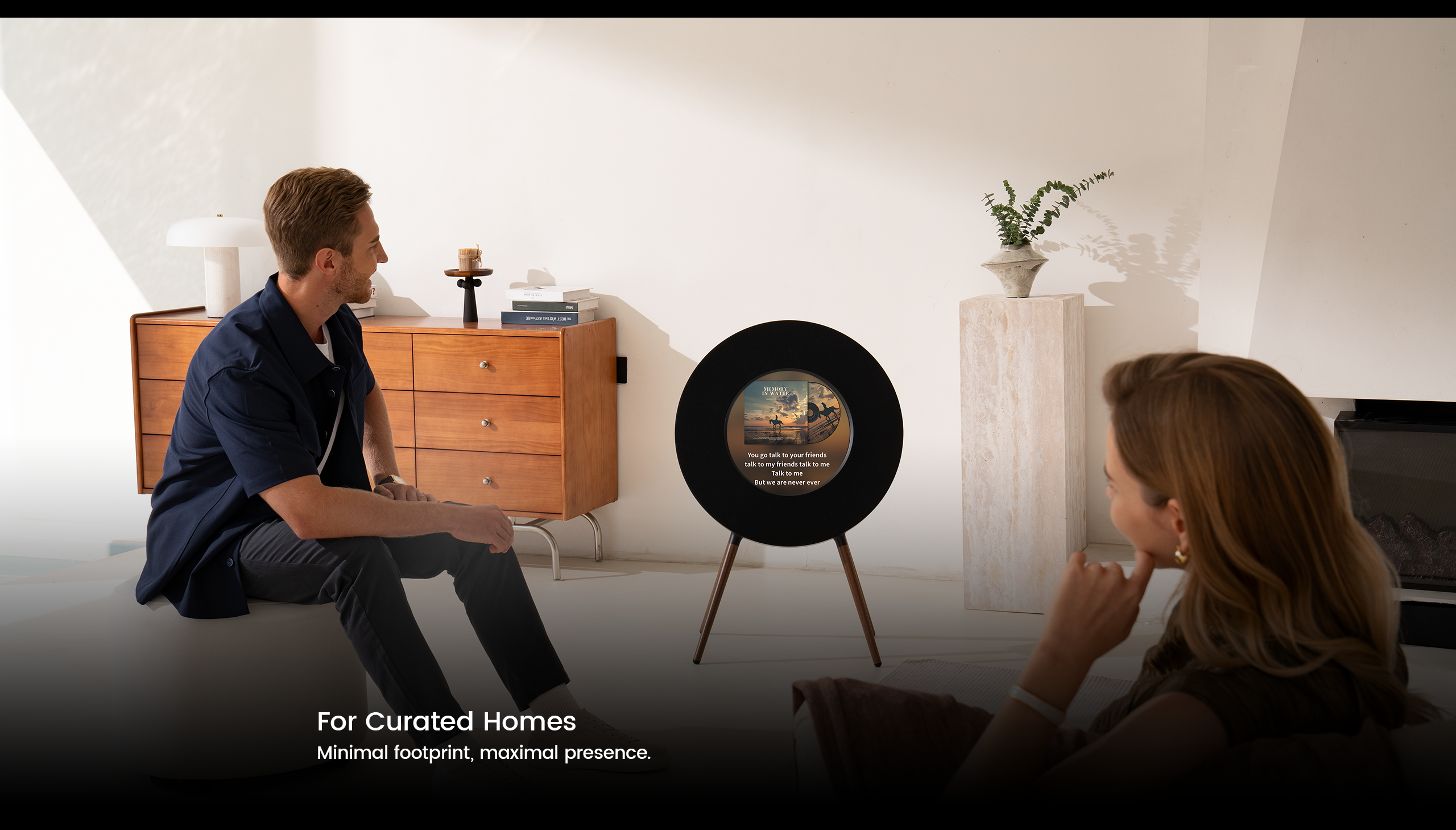 Two people sitting in a modern living room with a decorative item on a stand.