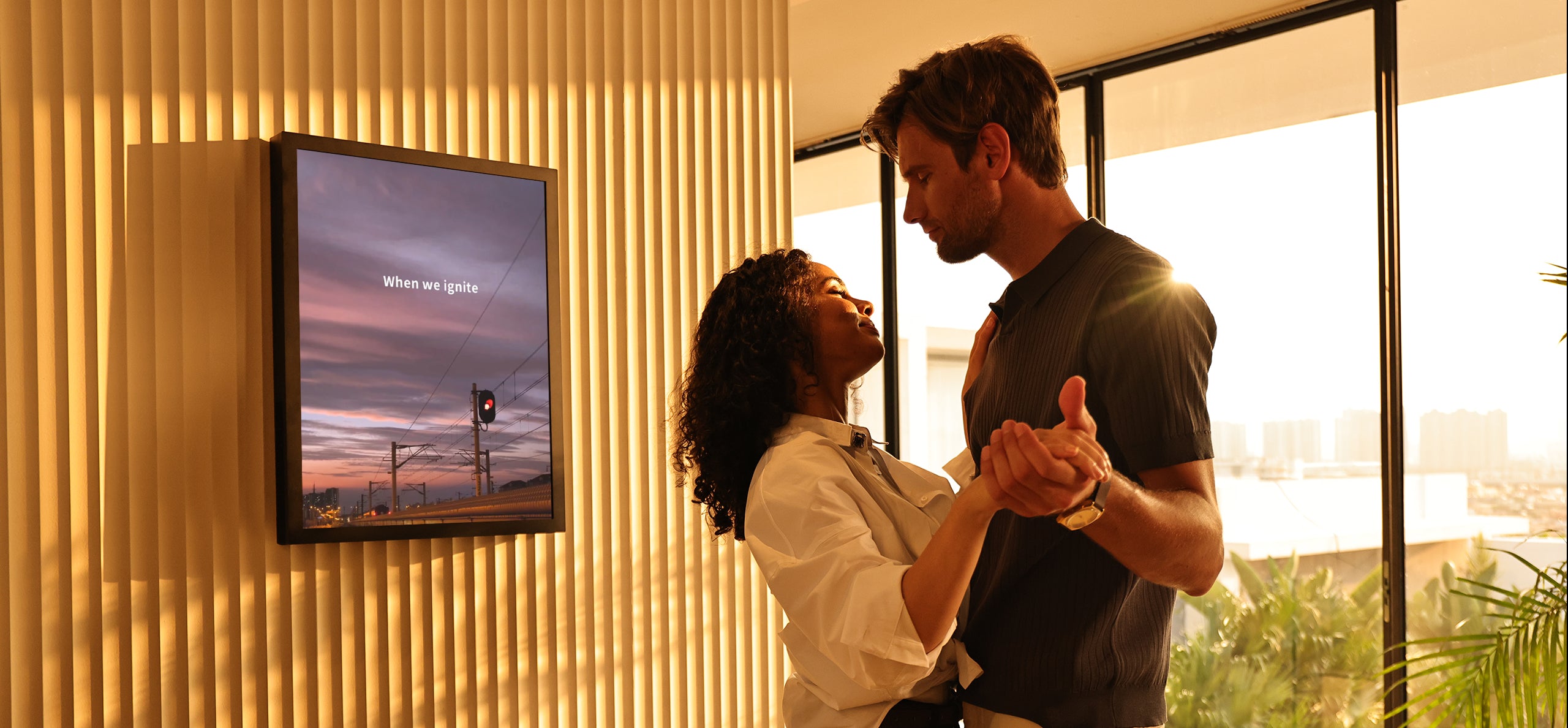 Two people embracing in a room with a television displaying a scenic image.